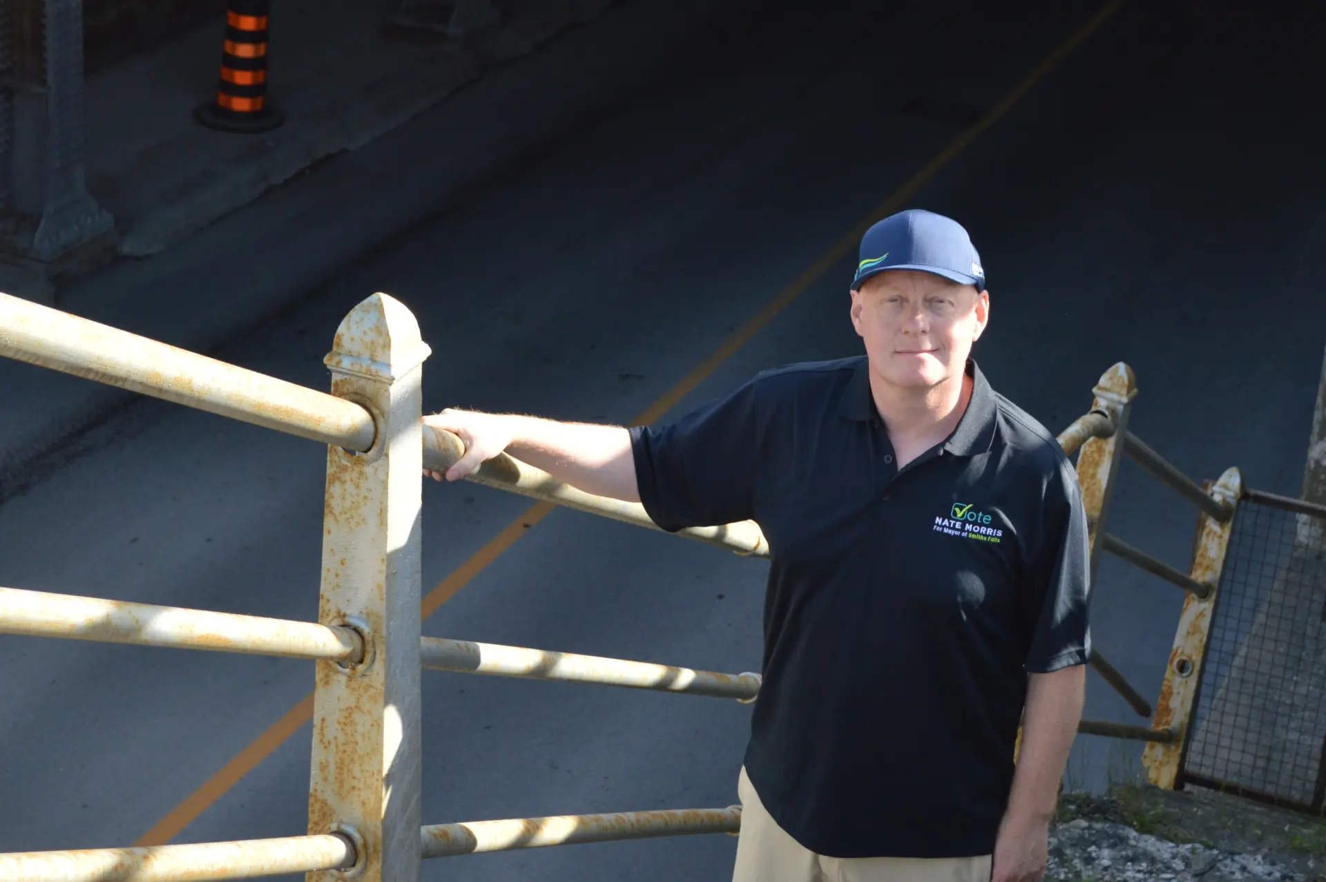 Nate Morris in his Vote Nate Morris campaign shirt and hat beside a railing in Smiths Falls