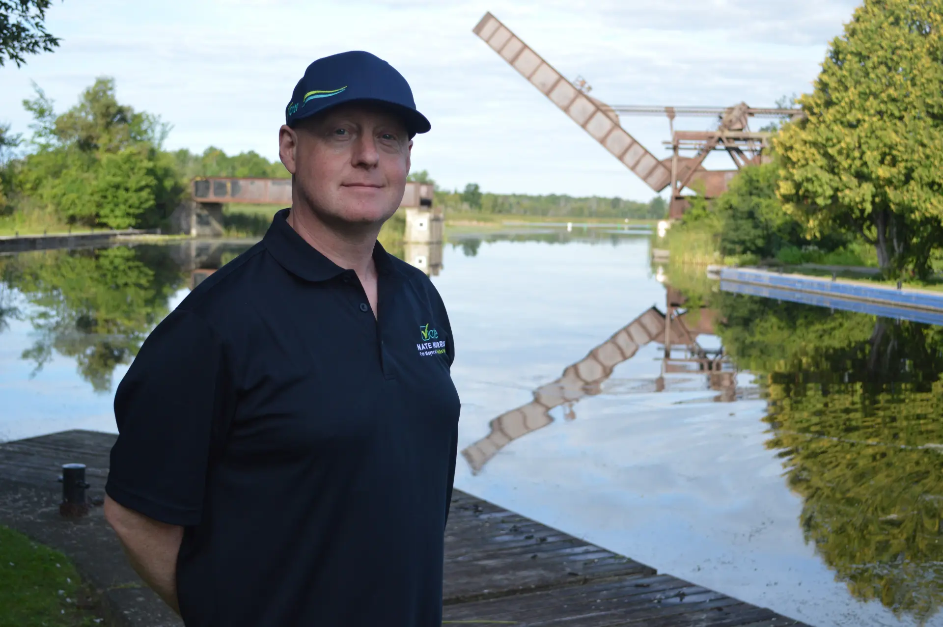 Nate Morris standing on the Rideau Canal waterfront in Smiths Falls with a railway bridge in the background.