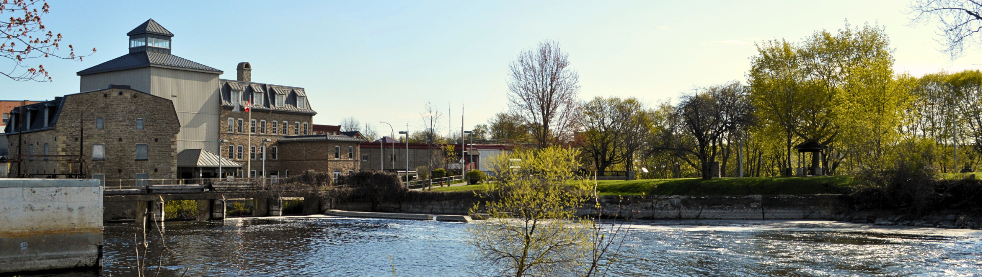 The Smiths Falls canal with historic stone mill buildings and trees lining the waterfront.